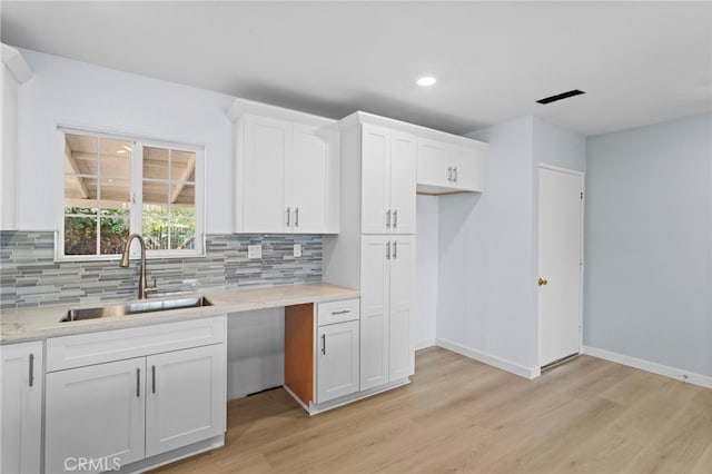 kitchen with light wood-style floors, white cabinetry, a sink, and backsplash