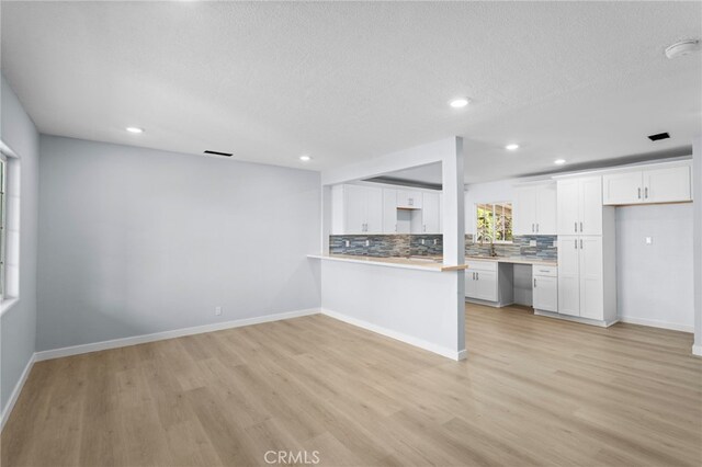 kitchen featuring tasteful backsplash, light countertops, white cabinetry, and light wood-style floors