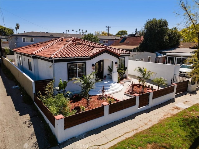 mediterranean / spanish-style home featuring a tile roof, stucco siding, fence private yard, and a garden