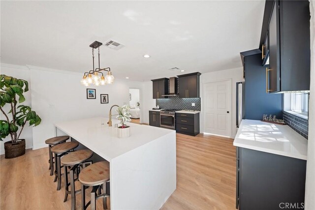 kitchen with stainless steel range with gas stovetop, light countertops, a kitchen breakfast bar, wall chimney range hood, and backsplash