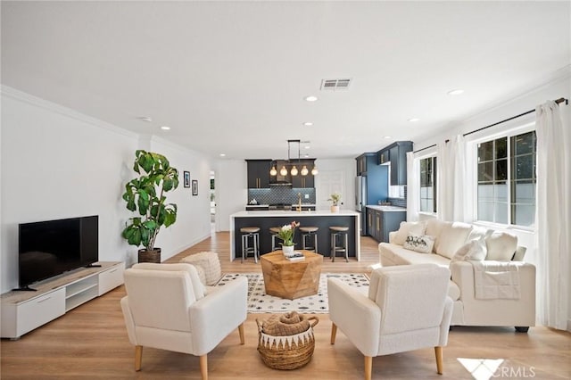 living room featuring visible vents, ornamental molding, and light wood-style flooring