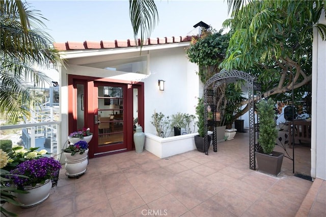 view of exterior entry featuring a tile roof, a patio area, and stucco siding