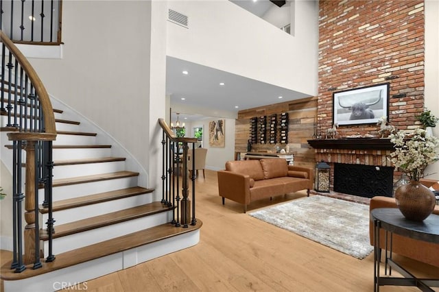 living room featuring a fireplace, a towering ceiling, visible vents, stairway, and wood finished floors
