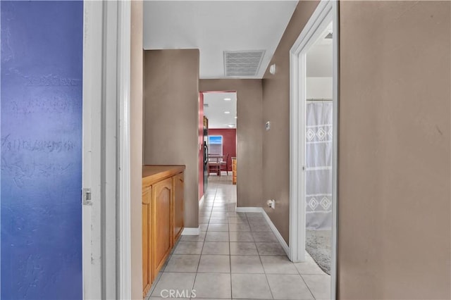 hall featuring baseboards, visible vents, and light tile patterned flooring