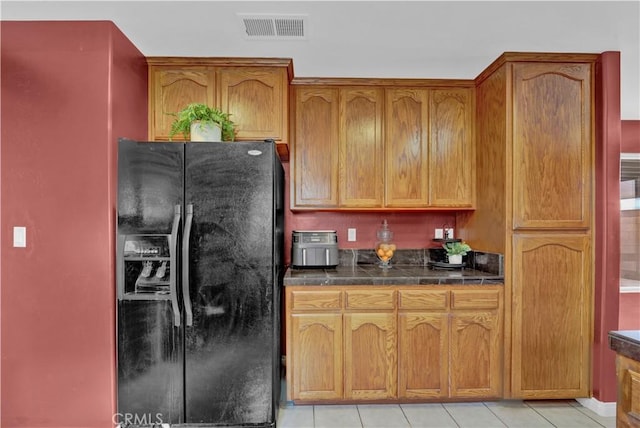 kitchen featuring light tile patterned flooring, visible vents, brown cabinets, and black fridge