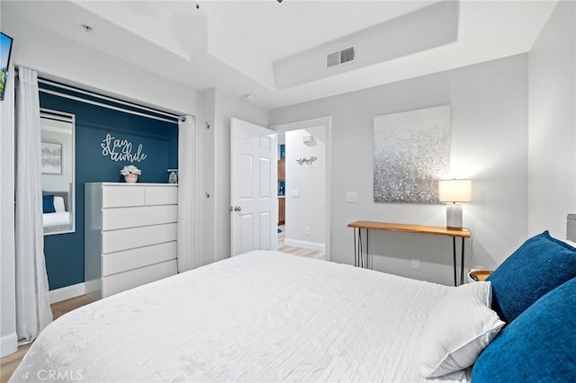 bedroom with visible vents, a raised ceiling, baseboards, and wood finished floors