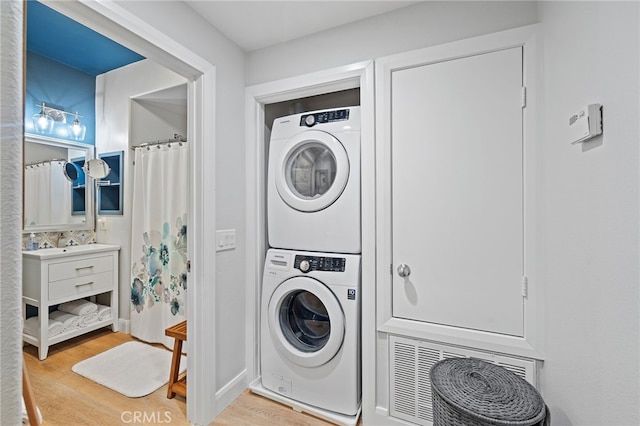 laundry area featuring stacked washer / drying machine, light wood finished floors, and laundry area