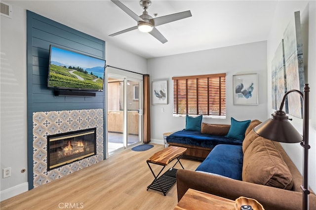 living area with visible vents, wood finished floors, baseboards, a tiled fireplace, and a ceiling fan
