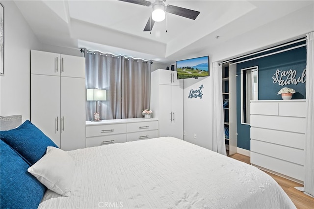 bedroom with ceiling fan, a raised ceiling, and light wood-type flooring
