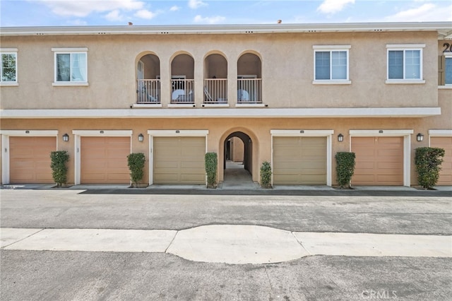 townhome / multi-family property with a garage, a balcony, and stucco siding