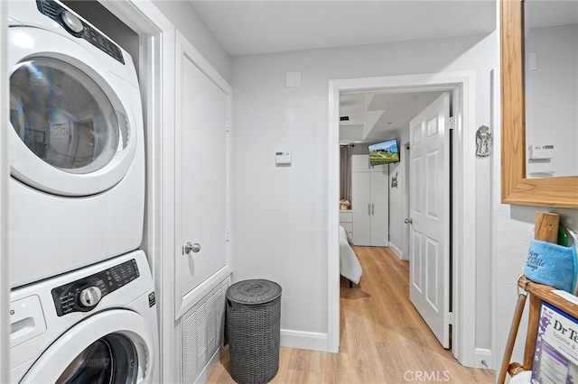 washroom with stacked washer / drying machine, baseboards, laundry area, and light wood-type flooring