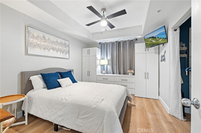 bedroom featuring a tray ceiling, ceiling fan, and light wood-style flooring