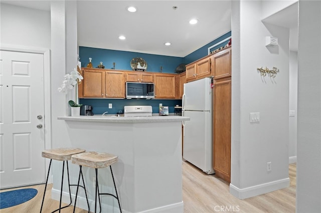 kitchen with light wood finished floors, range, freestanding refrigerator, a peninsula, and stainless steel microwave