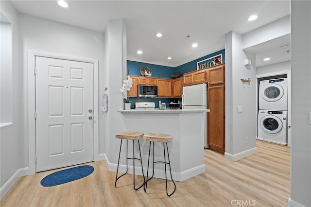 kitchen featuring range, stainless steel microwave, freestanding refrigerator, stacked washer and clothes dryer, and light wood-style flooring