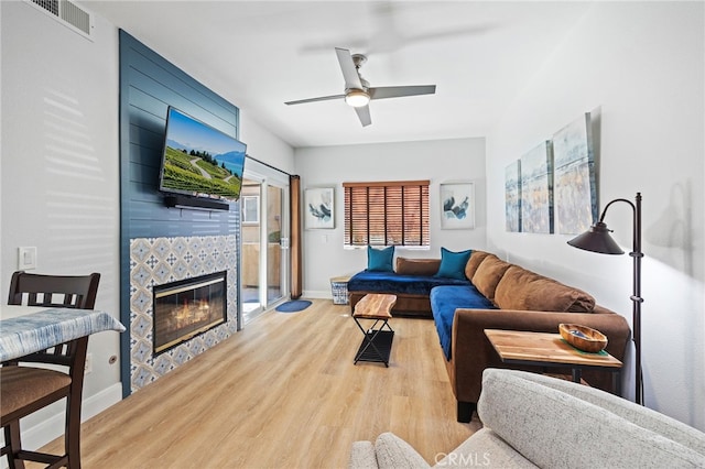 living room with ceiling fan, visible vents, a tiled fireplace, baseboards, and light wood-style flooring