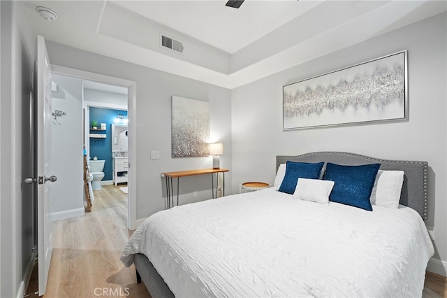 bedroom featuring baseboards, a tray ceiling, visible vents, and wood finished floors