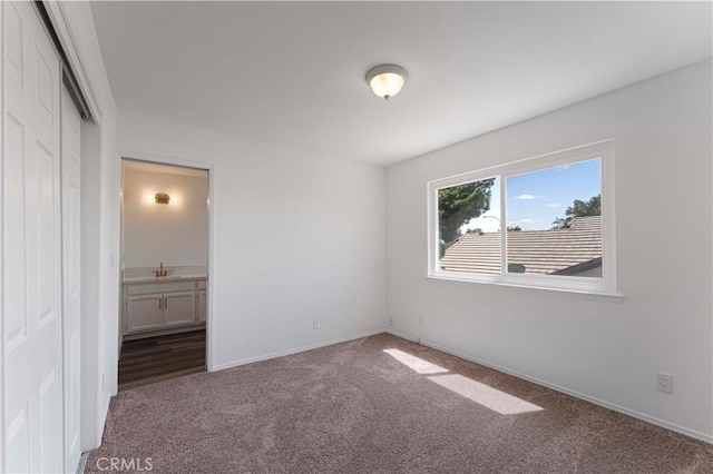 unfurnished bedroom featuring baseboards, carpet flooring, a sink, and a closet