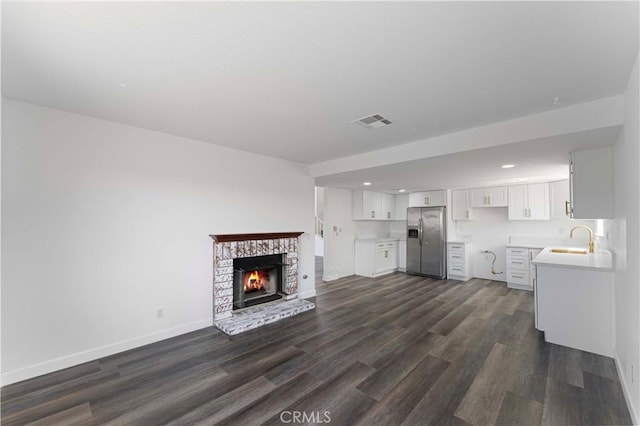 unfurnished living room featuring visible vents, recessed lighting, a sink, and dark wood-style flooring
