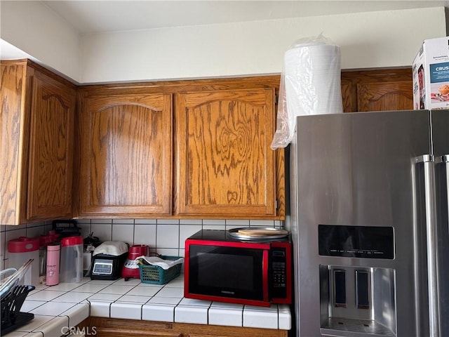 3816 Phaffle Dr, Bakersfield, CA 93309 - kitchen featuring stainless steel refrigerator with ice dispenser, tile counters, brown cabinetry, and backsplash