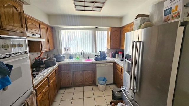 3816 Phaffle Dr, Bakersfield, CA 93309 - kitchen with white appliances, tile counters, brown cabinetry, under cabinet range hood, and light tile patterned flooring