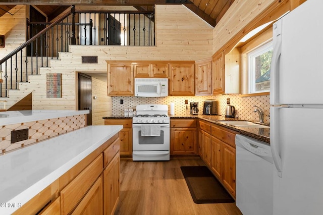 kitchen featuring wooden walls, white appliances, wood finished floors, and a sink