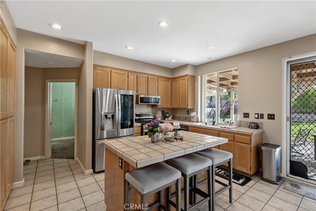kitchen featuring a sink, a kitchen island, tile countertops, appliances with stainless steel finishes, and light tile patterned flooring