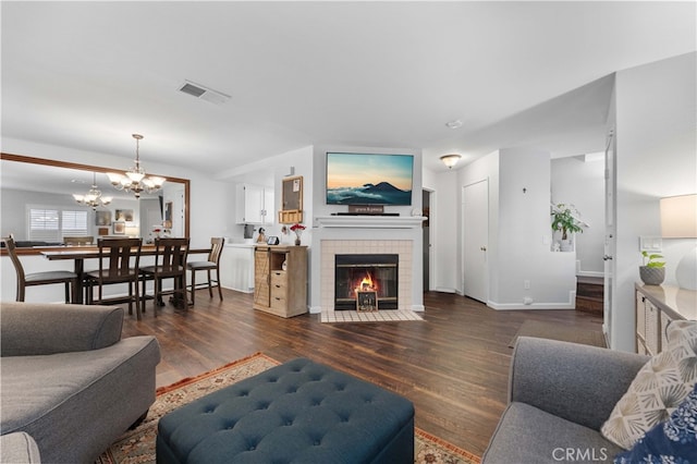 living room with visible vents, dark wood finished floors, a fireplace, baseboards, and a chandelier