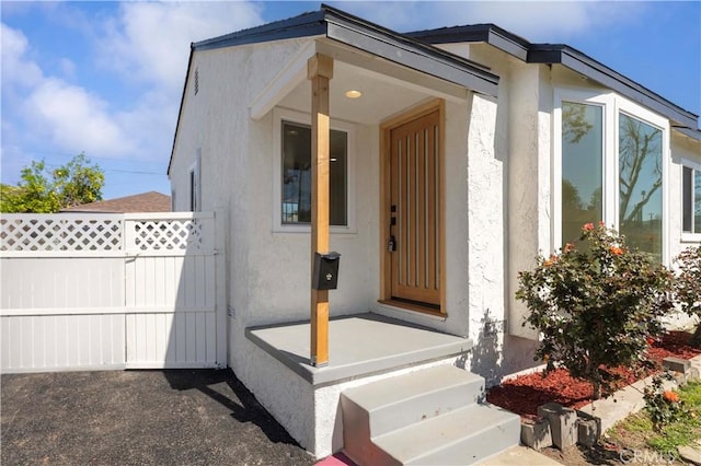 doorway to property featuring stucco siding and fence
