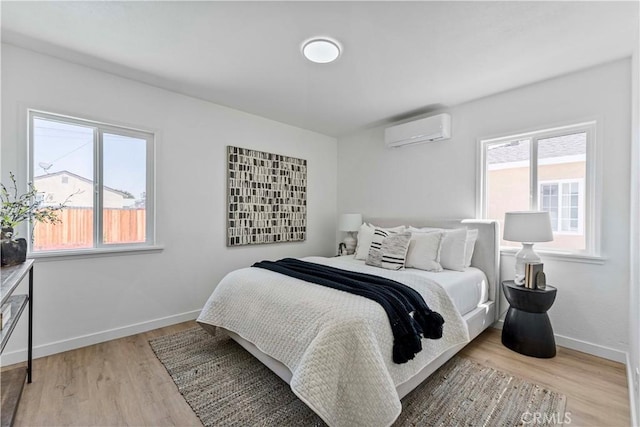 bedroom with baseboards, multiple windows, wood finished floors, and a wall mounted air conditioner