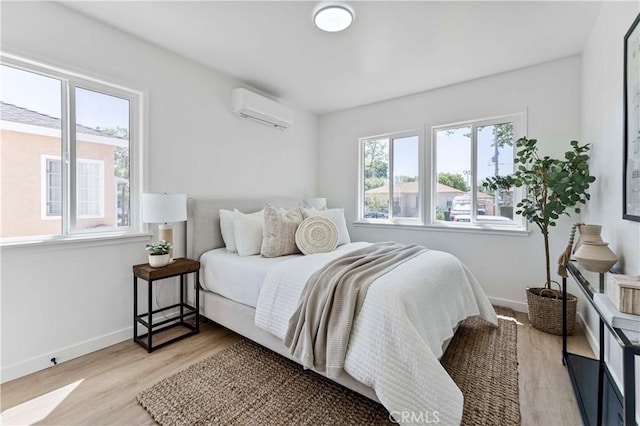 bedroom featuring baseboards, light wood-type flooring, and a wall mounted AC