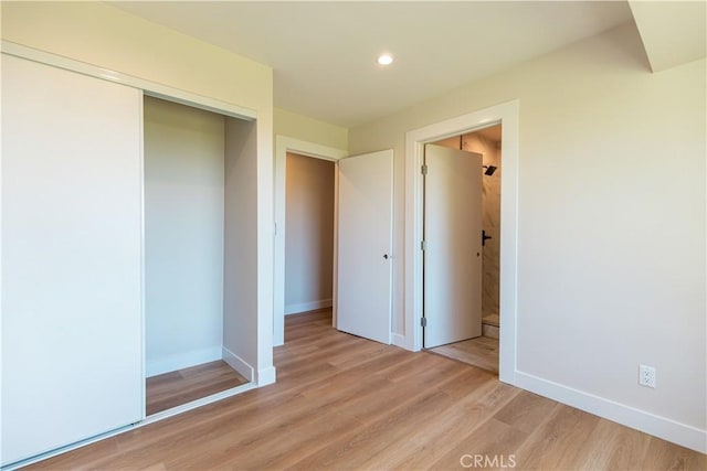 unfurnished bedroom with recessed lighting, light wood-type flooring, ensuite bathroom, baseboards, and a closet