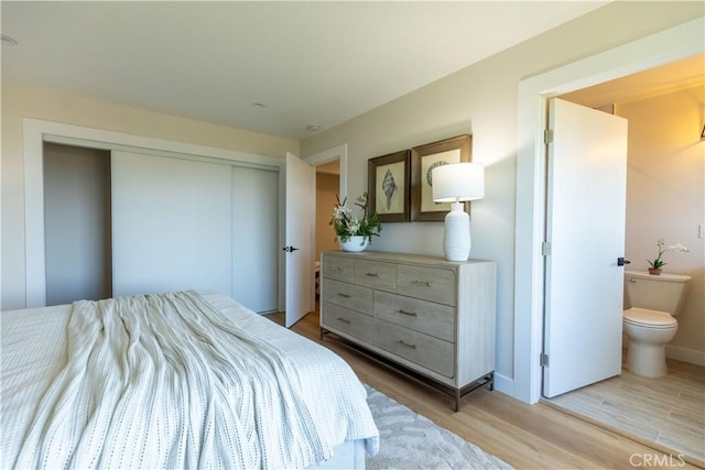 bedroom with a closet, ensuite bath, baseboards, and light wood finished floors