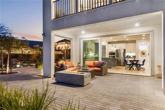 patio terrace at dusk with an outdoor living space with a fire pit and a balcony