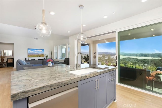 kitchen with stainless steel dishwasher, a sink, light wood-type flooring, pendant lighting, and light stone countertops