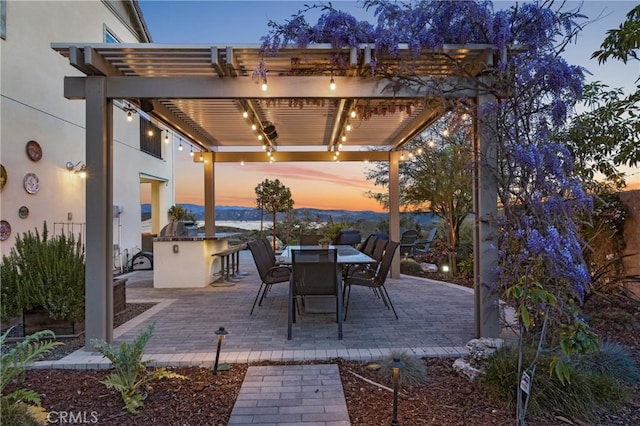 patio terrace at dusk featuring a pergola, outdoor dining space, and exterior kitchen