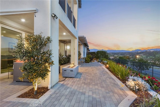 patio terrace at dusk featuring a fire pit, fence, and a mountain view