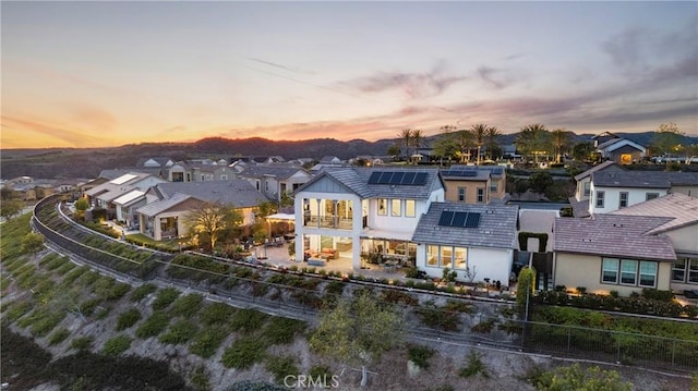 back of property at dusk featuring a residential view, a fenced backyard, roof mounted solar panels, a patio, and stucco siding