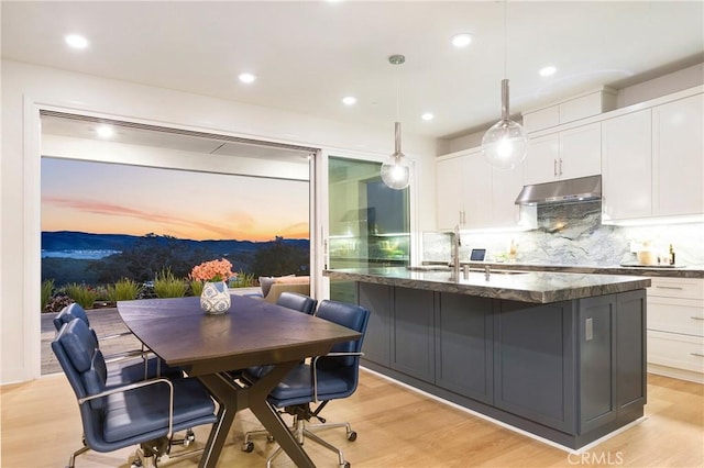kitchen with white cabinets, under cabinet range hood, backsplash, a sink, and dark stone counters