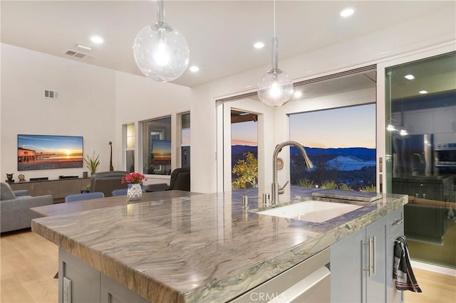 kitchen featuring a center island with sink, stone countertops, a sink, and visible vents