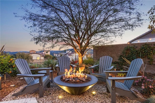 patio terrace at dusk featuring an outdoor fire pit and fence