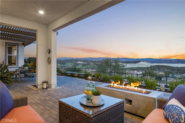 patio terrace at dusk with a pergola, an outdoor fire pit, outdoor dining space, and a mountain view
