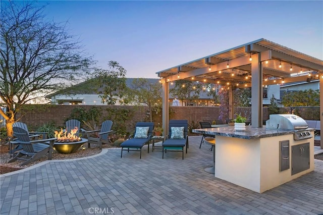 patio terrace at dusk featuring exterior kitchen, outdoor dry bar, a fire pit, and fence