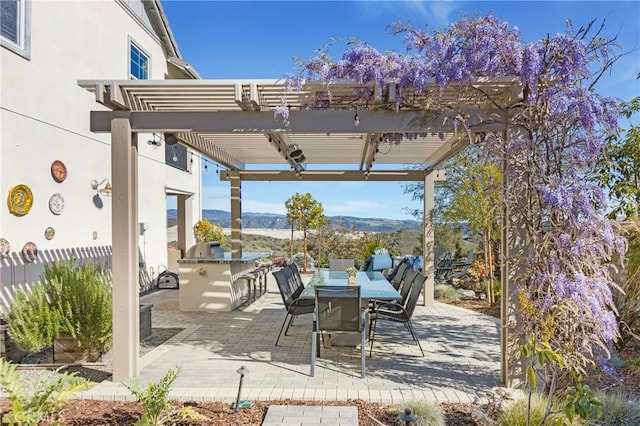 view of patio / terrace with an outdoor kitchen, exterior bar, a pergola, outdoor dining space, and a mountain view