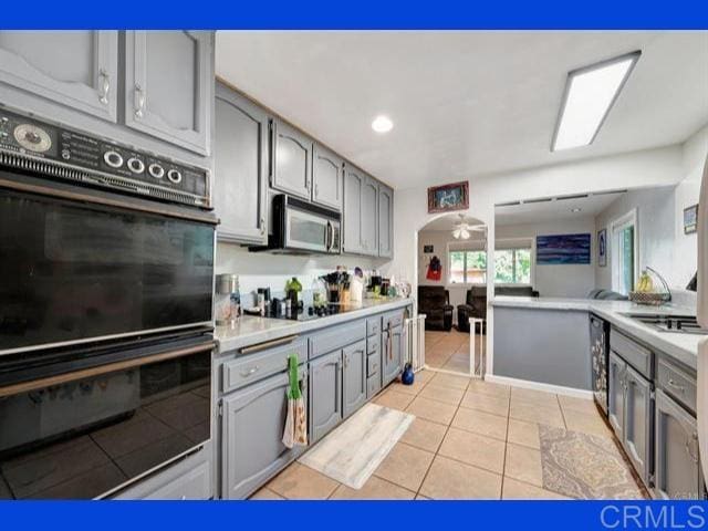 kitchen featuring black appliances, light tile patterned flooring, gray cabinetry, and light countertops