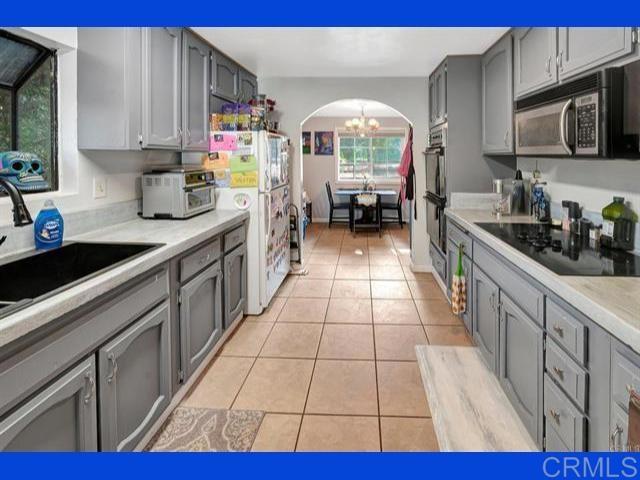 kitchen featuring gray cabinetry, light tile patterned floors, arched walkways, a notable chandelier, and black appliances