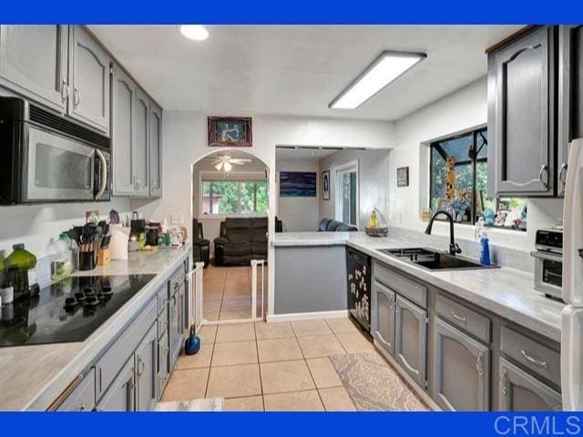 kitchen with gray cabinetry, light countertops, light tile patterned floors, black appliances, and a sink
