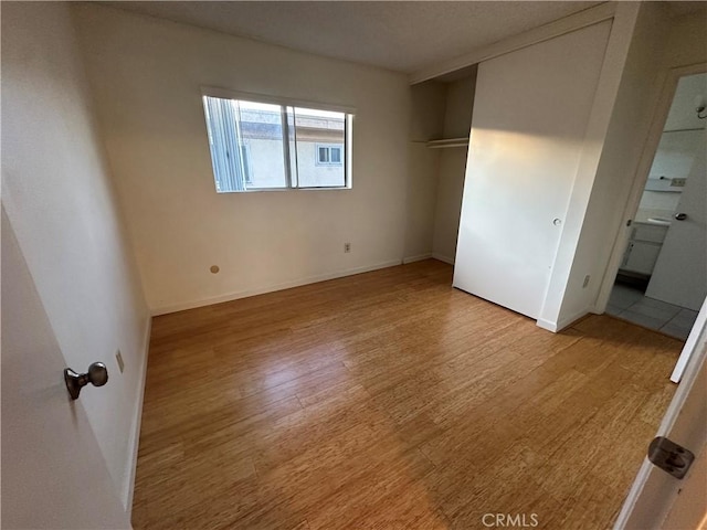 unfurnished bedroom with light wood finished floors, baseboards, connected bathroom, and a closet