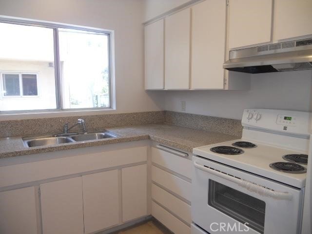 kitchen with white electric stove, white cabinetry, under cabinet range hood, and a sink