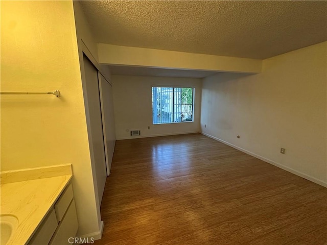 unfurnished bedroom featuring a textured ceiling, wood finished floors, visible vents, and baseboards