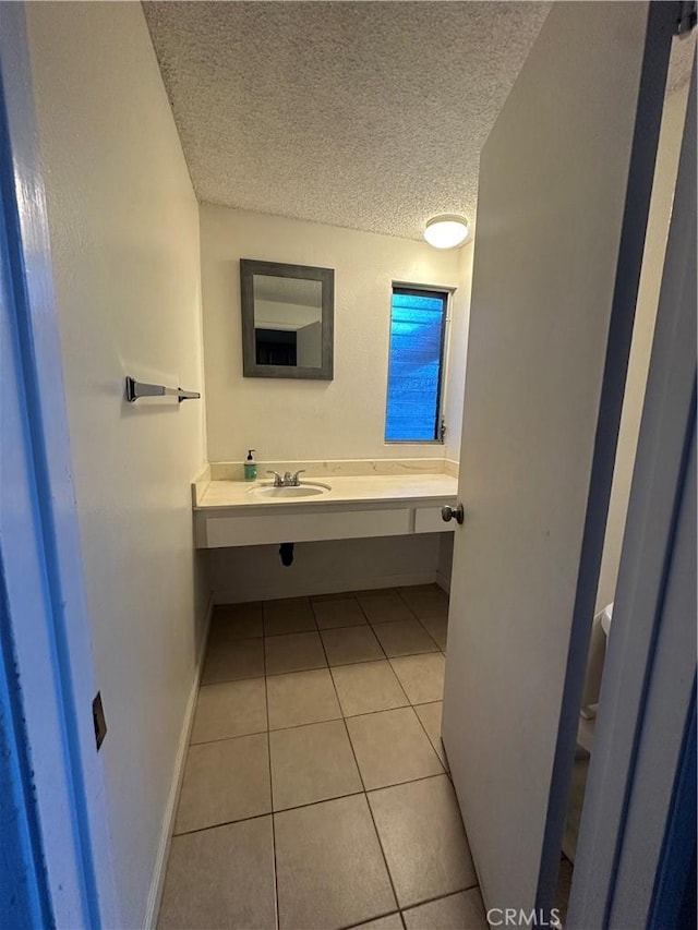 bathroom featuring a textured ceiling, tile patterned flooring, baseboards, and a sink
